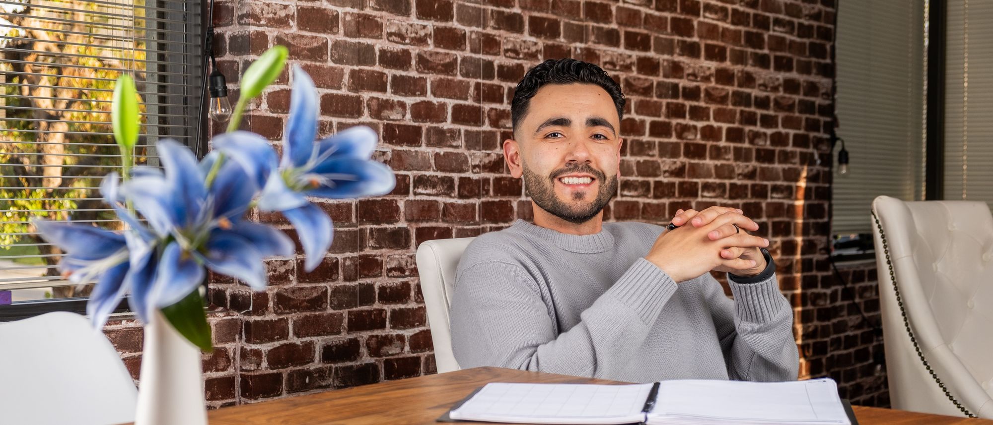 Chafik at a table with an open notebook, hands clasped, smiling